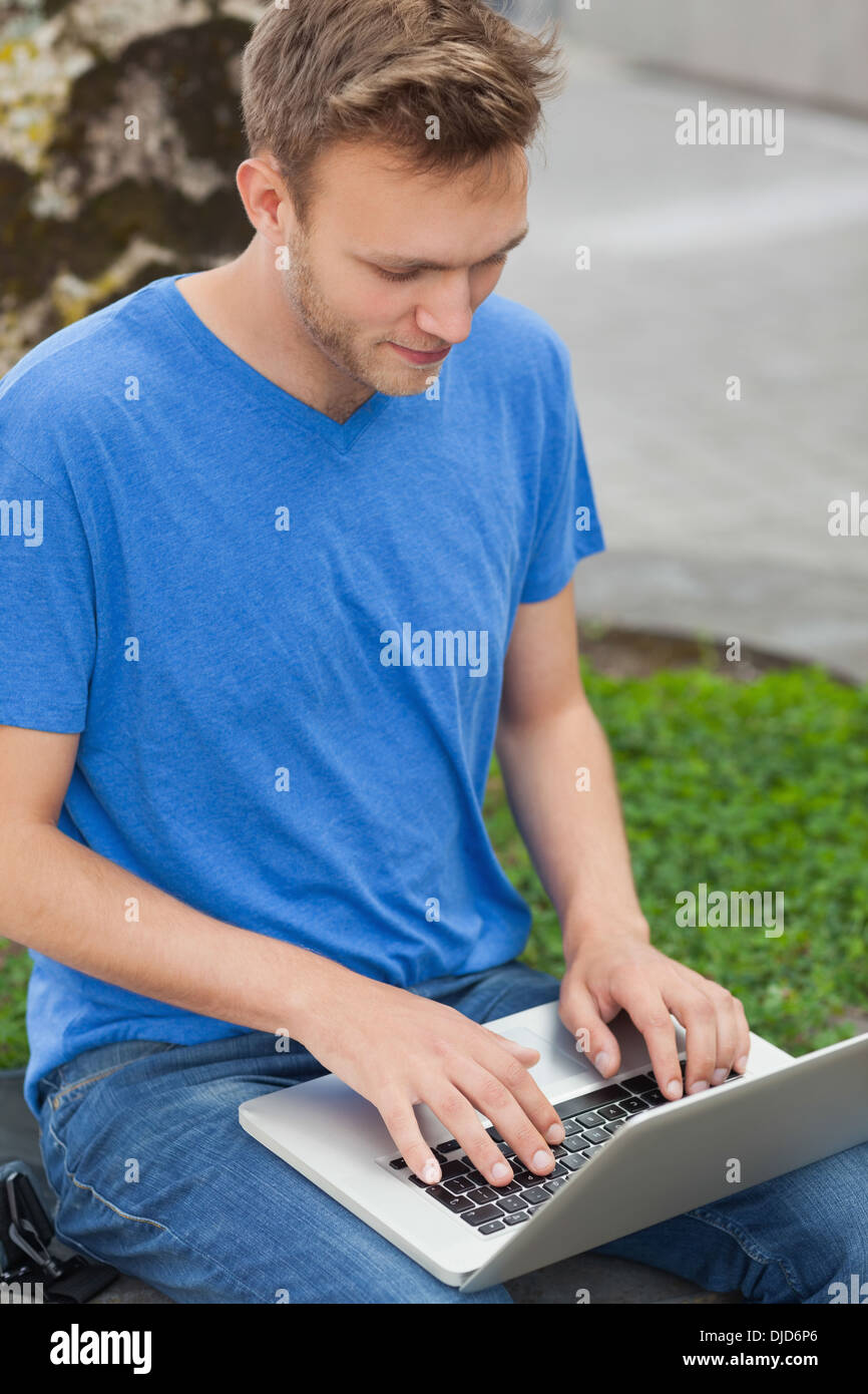Peaceful handsome student sitting on wall studying Stock Photo