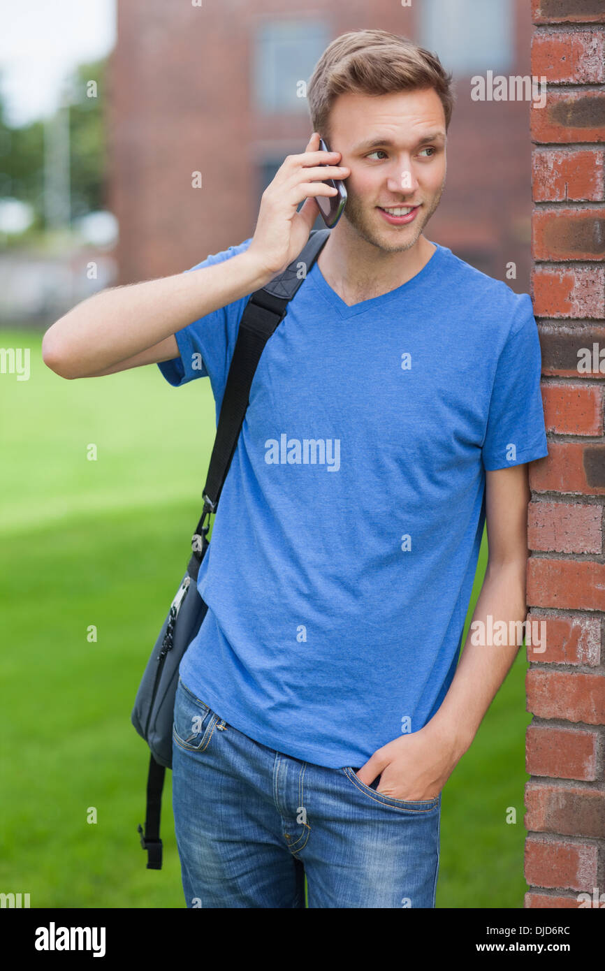 Happy handsome student leaning against wall phoning Stock Photo