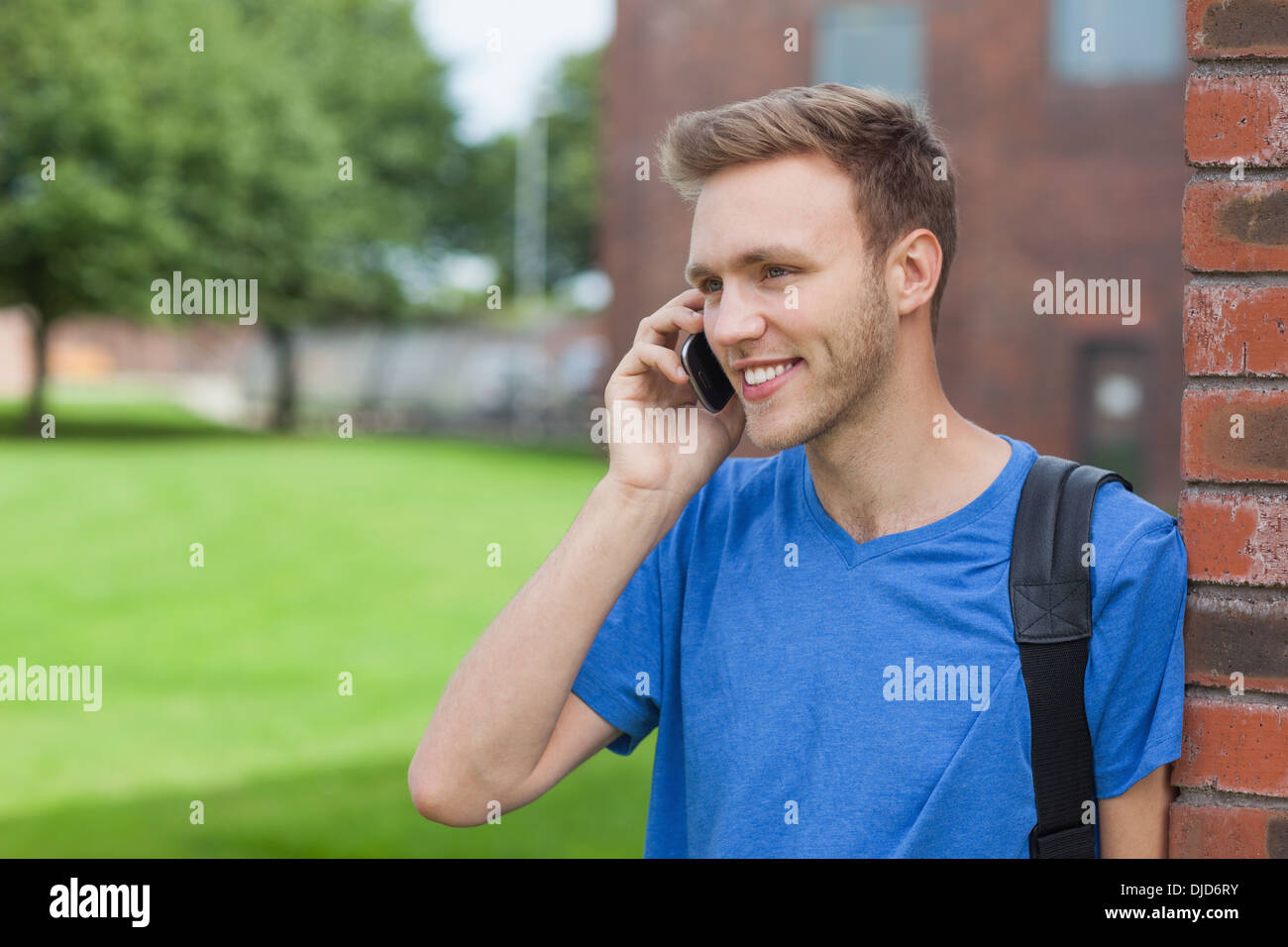 Smiling handsome student leaning against wall phoning Stock Photo