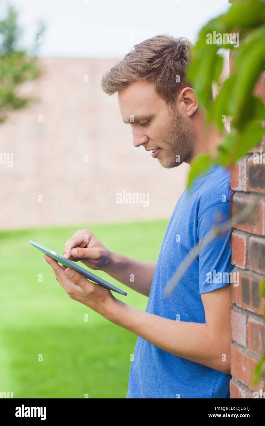 Happy handsome student leaning against wall using tablet Stock Photo