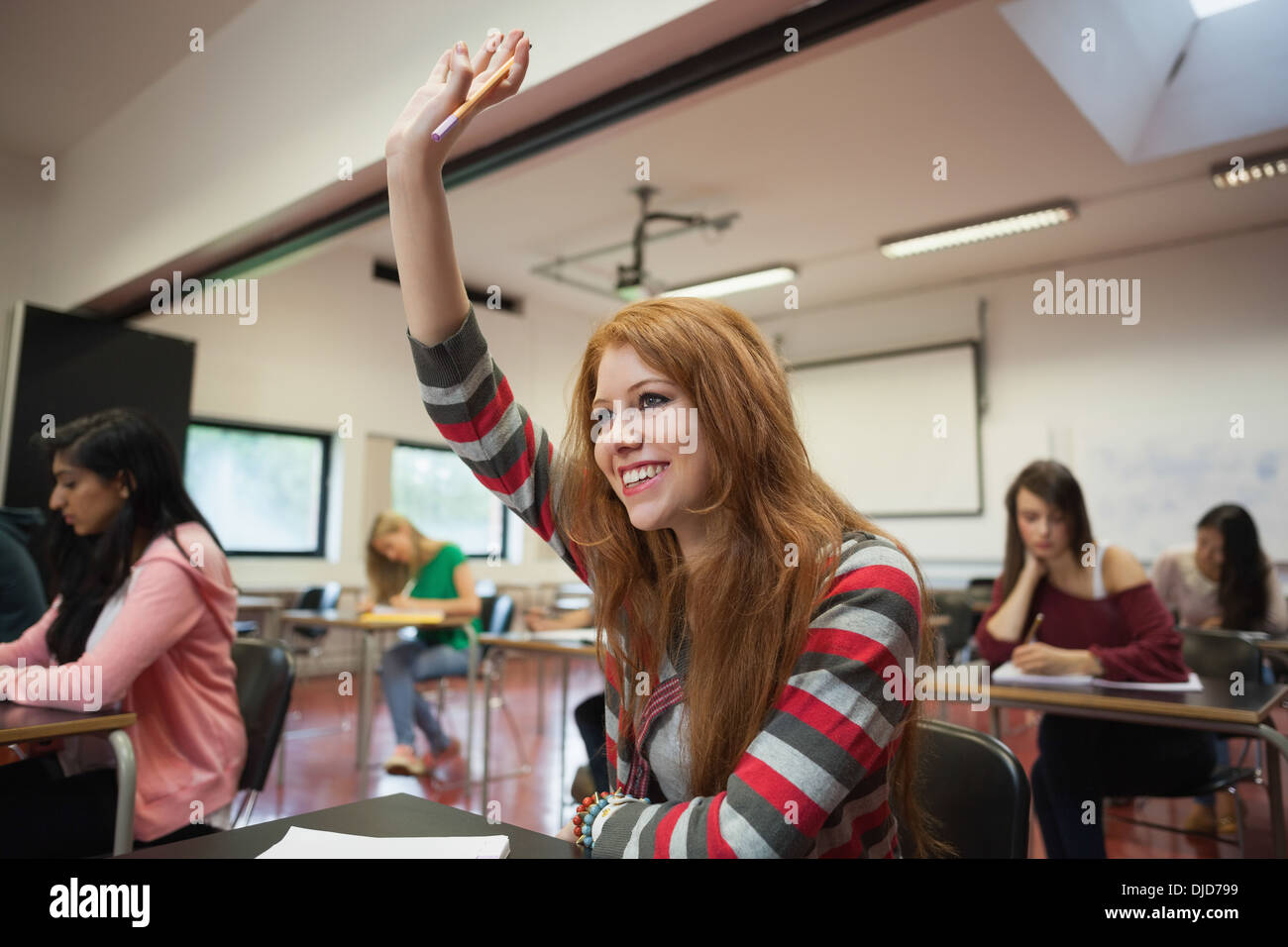 Smiling female student raising her hand in class Stock Photo