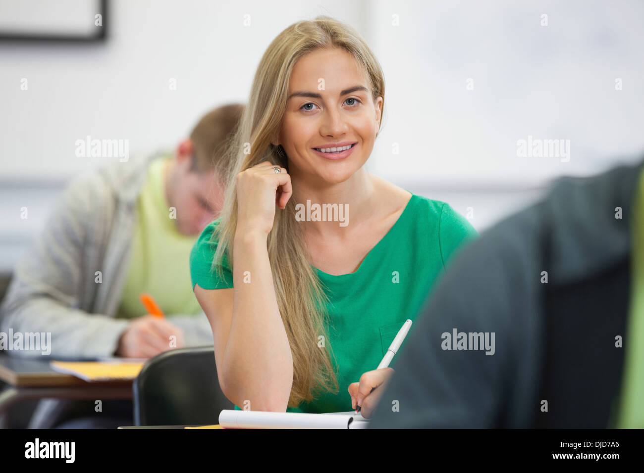 Pretty blonde student taking notes in class smiling at camera Stock Photo