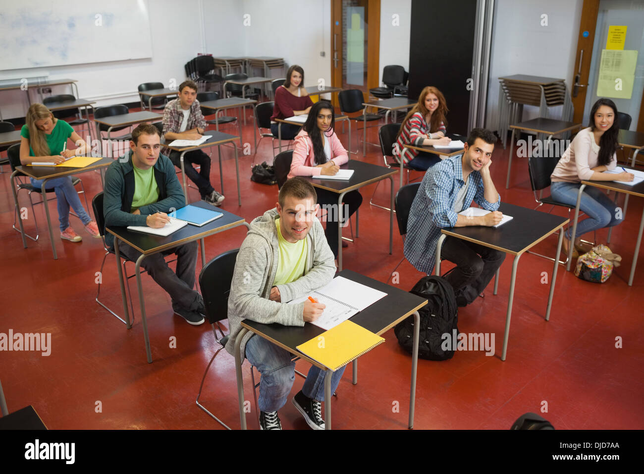 Students taking notes in class smiling up at camera Stock Photo