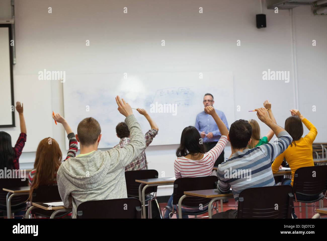 Students listening to their teacher in classroom and raising their hands Stock Photo