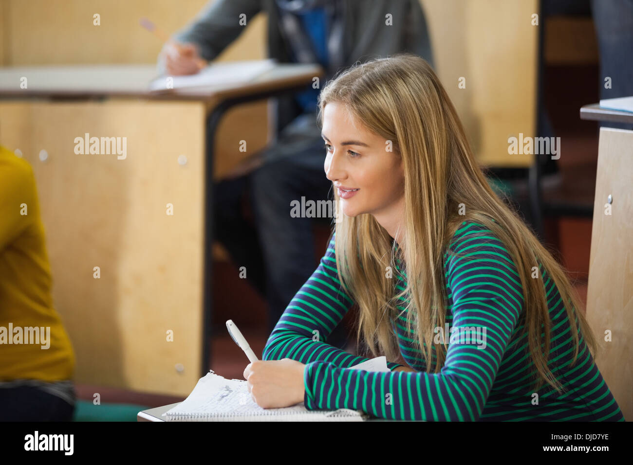 Smiling blonde student taking notes in a lecture hall Stock Photo