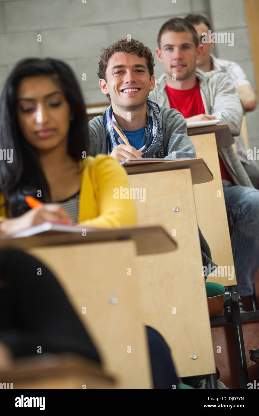 Smiling handsome student taking notes in a lecture hall Stock Photo
