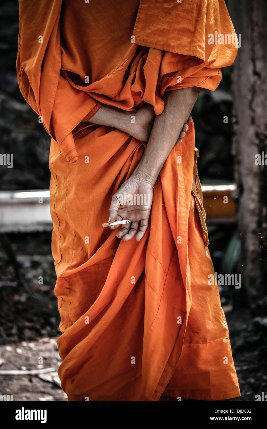 Thai monk smoking and concealing a cigarette behind his back. Thailand S. E. Asia Monk from behind Stock Photo