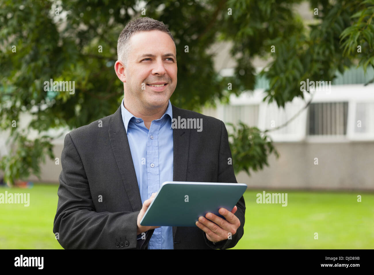 Smiling lecturer using his tablet pc outside on campus Stock Photo