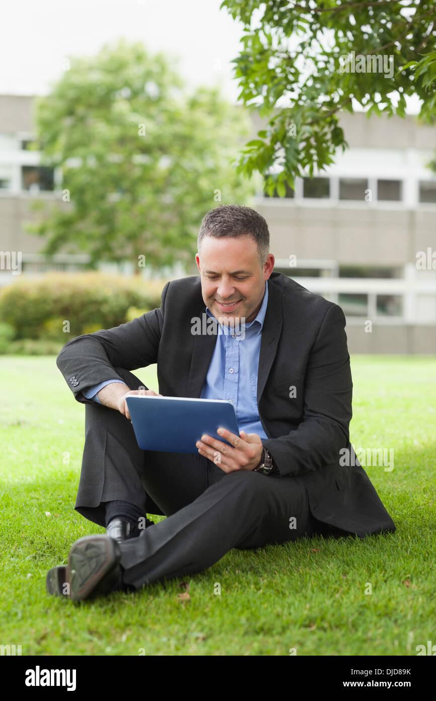 Happy lecturer using his tablet pc sitting outside on campus Stock Photo