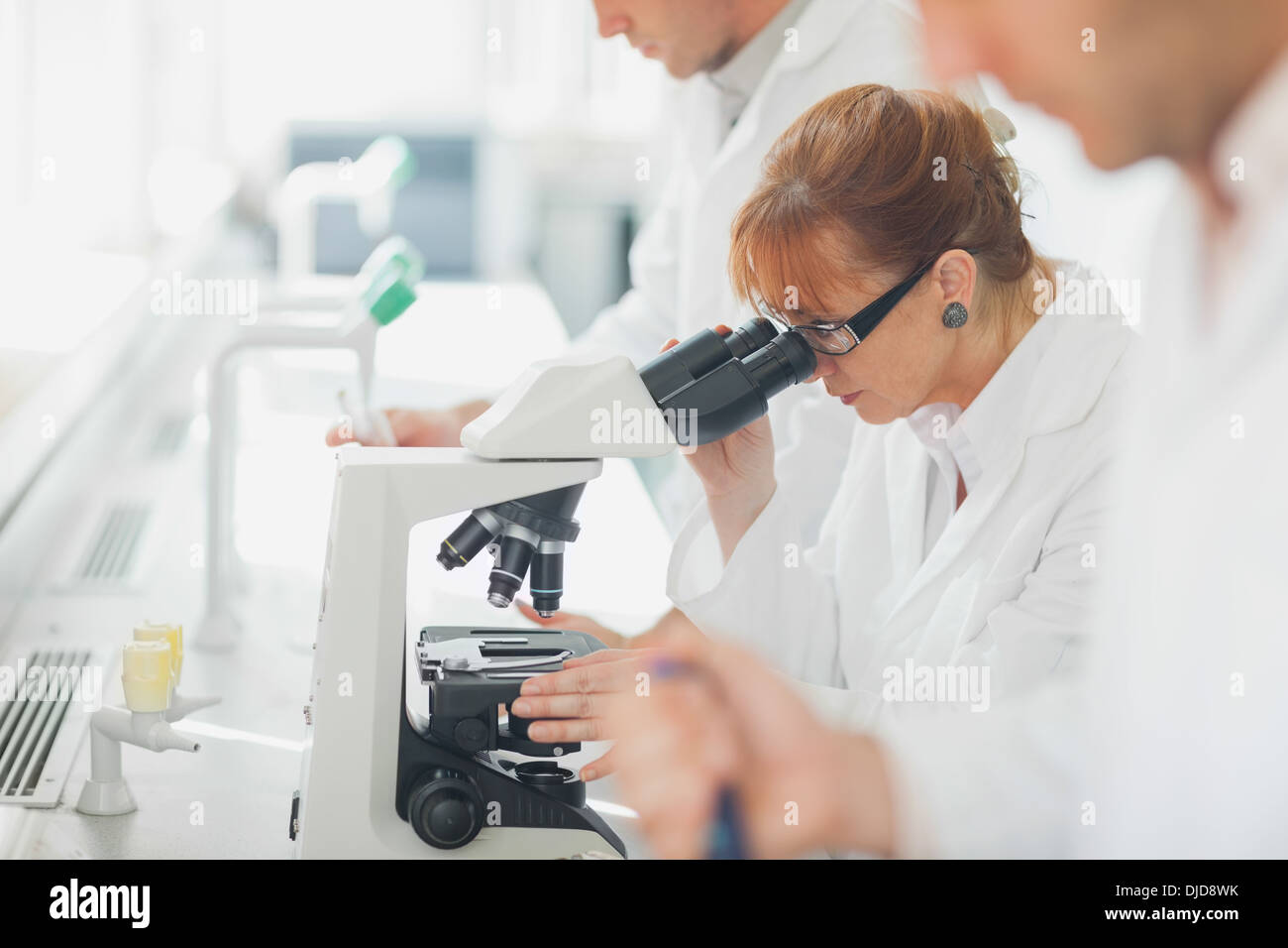 Female scientist wearing a lab coat looking through a microscope Stock Photo