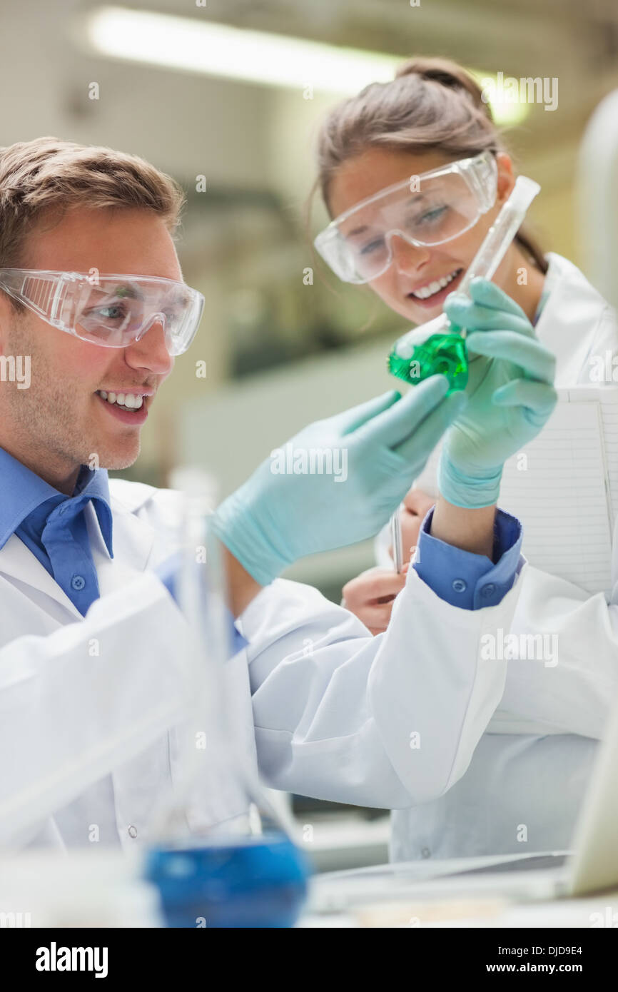 Two happy students looking at green liquid and taking notes Stock Photo