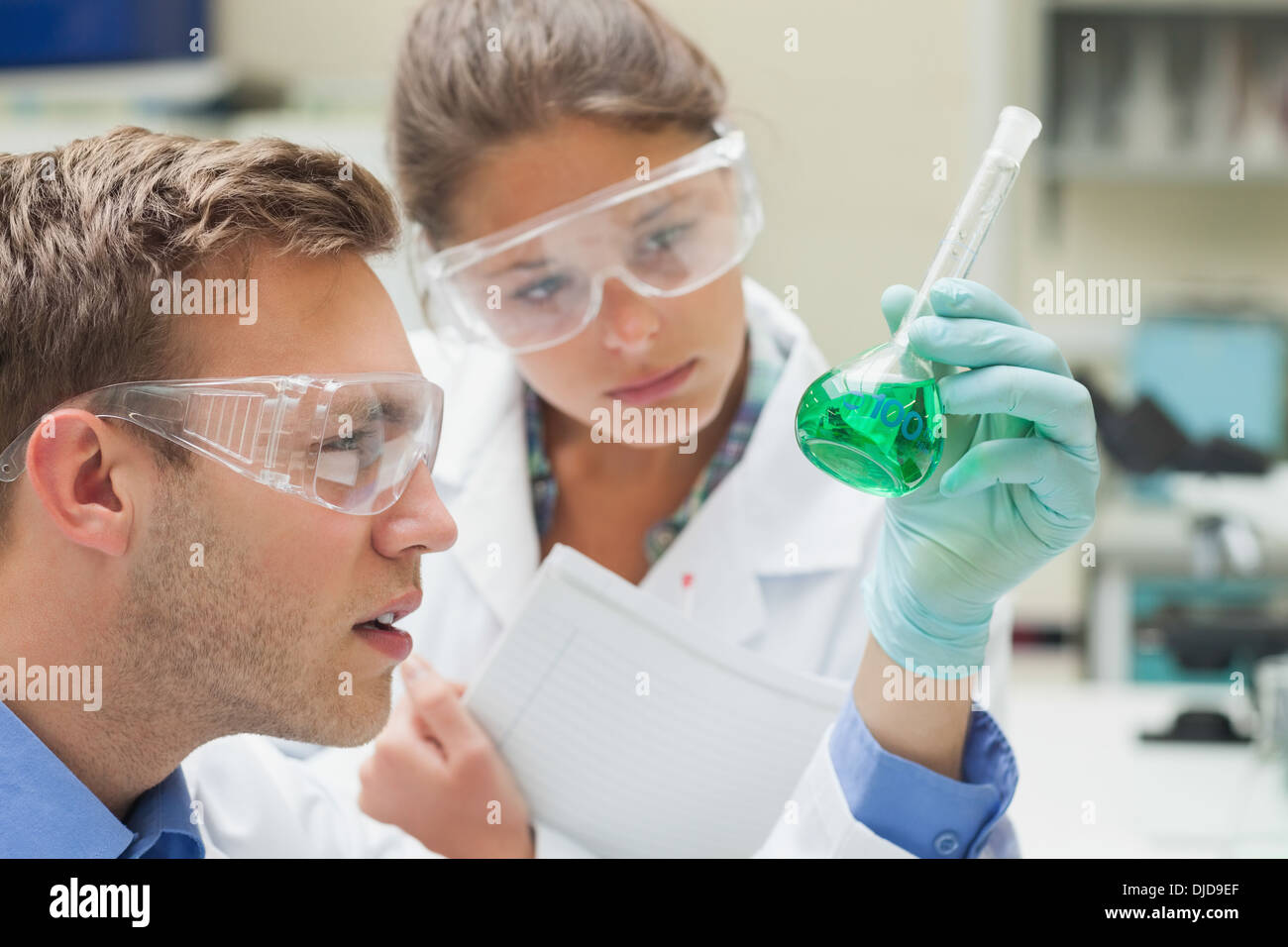 Two students looking closely at green liquid and taking notes Stock Photo