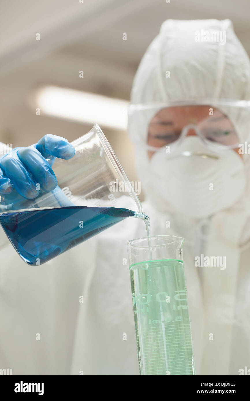 Lab assistant with mask pouring blue liquid in beaker Stock Photo