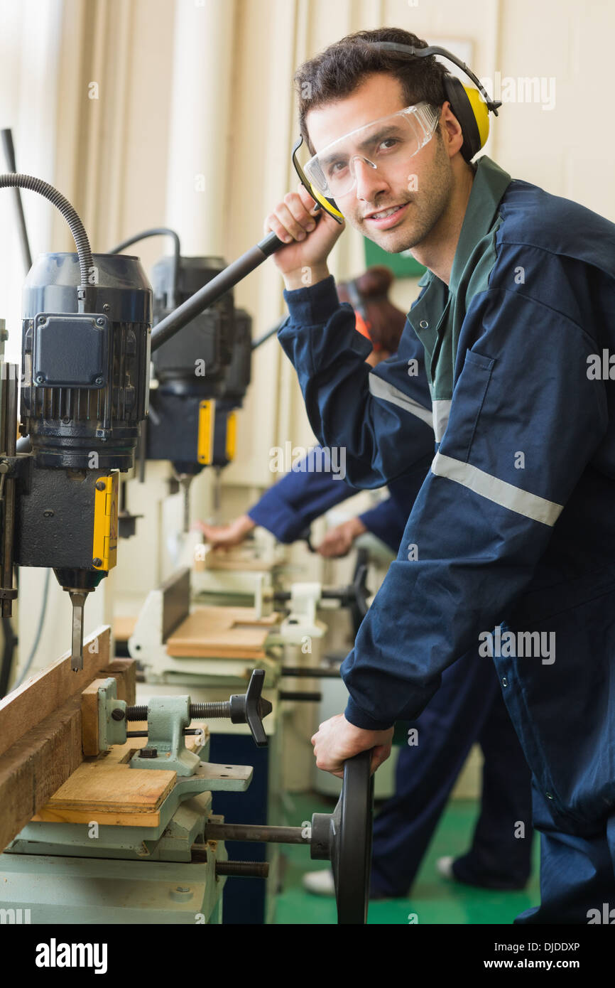Smiling craftsman with safety glasses drilling a piece of wood Stock