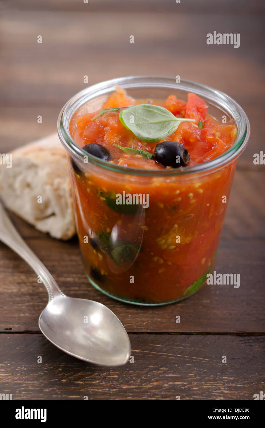 Jelly jar with tomato sauce, black olives and leaves of basil served