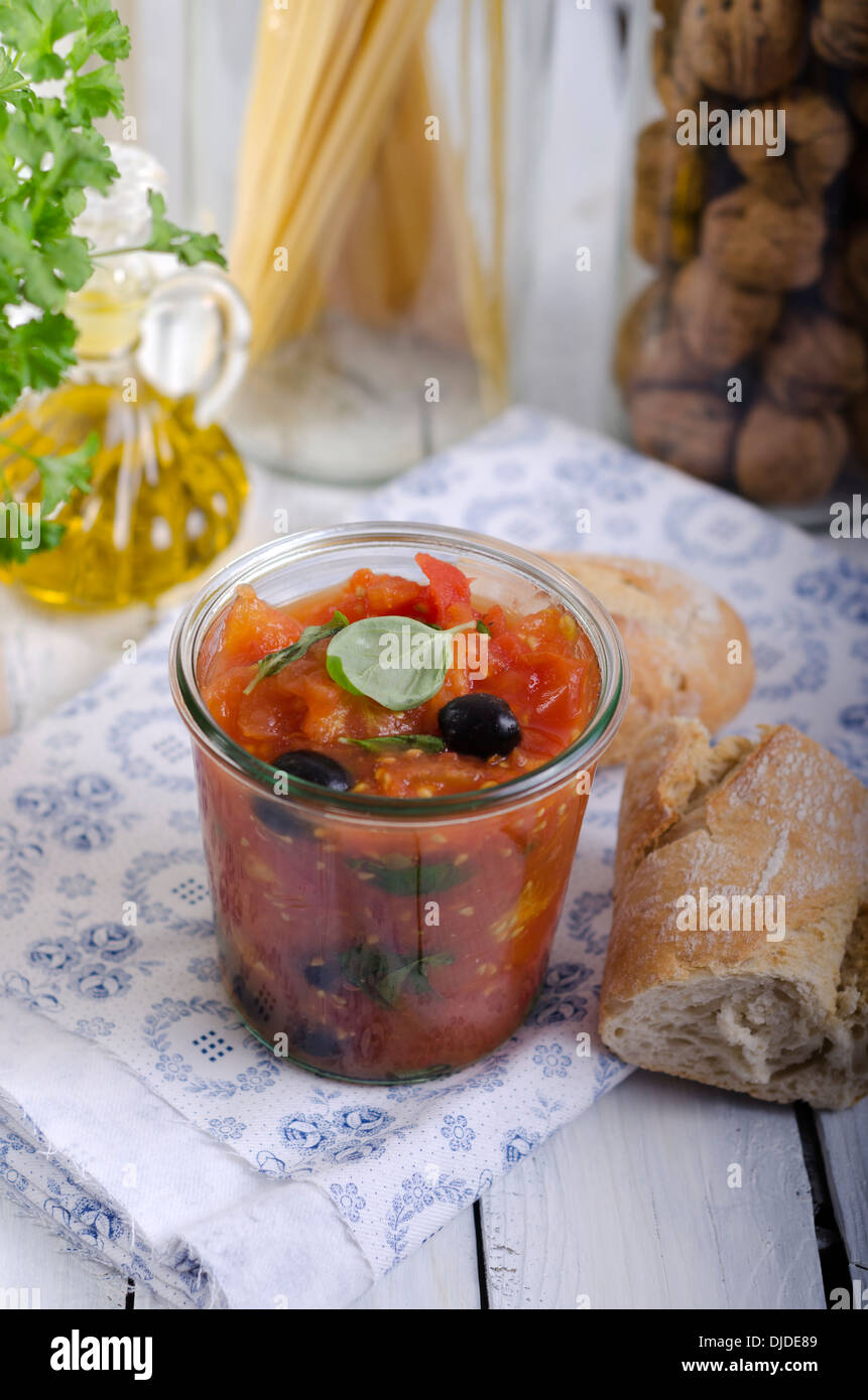 Jelly jar with tomato sauce, black olives and leaves of basil served