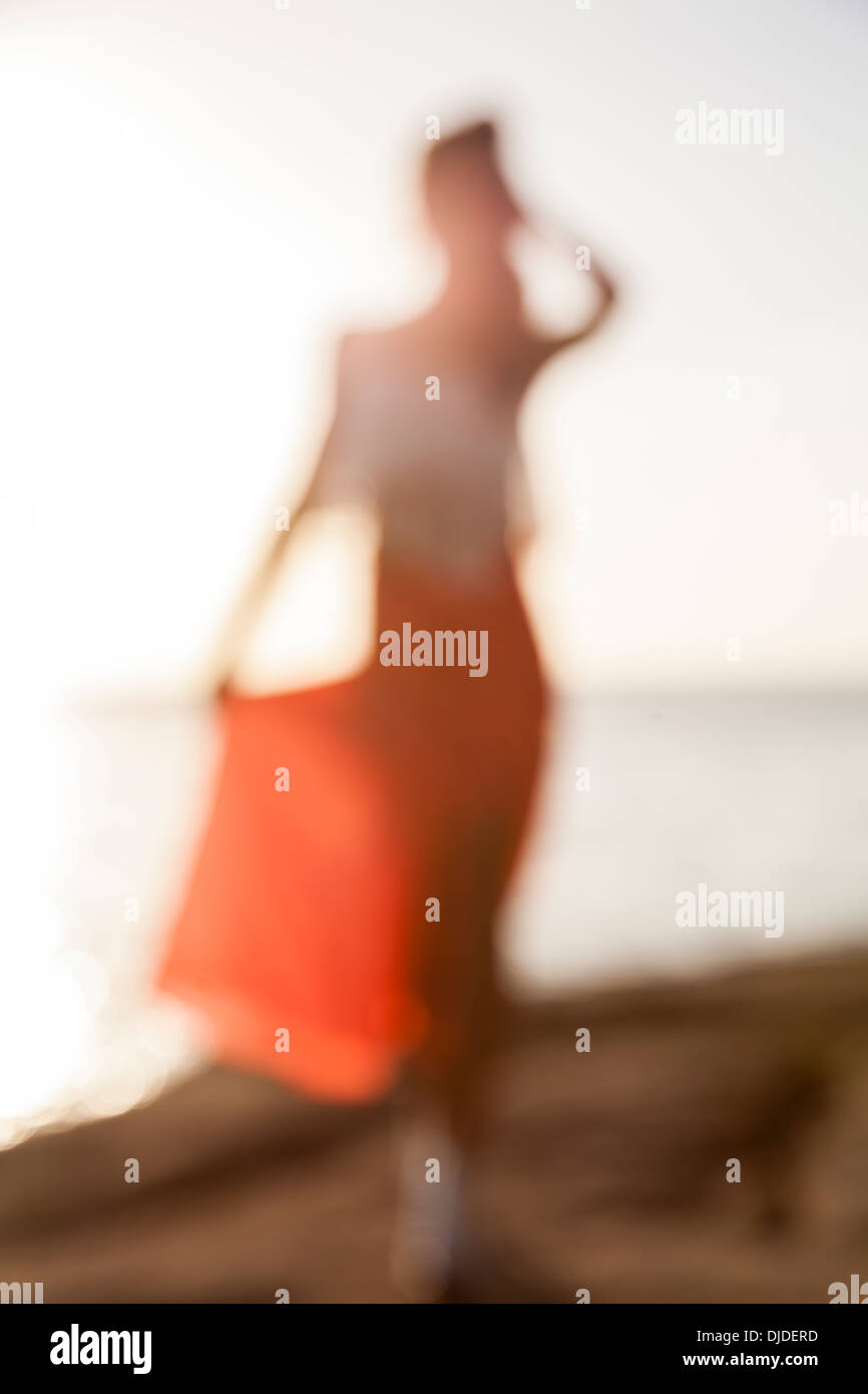 Blurred out of focus woman in red skirt and white top walking on cliff top with sea and sky in background Stock Photo