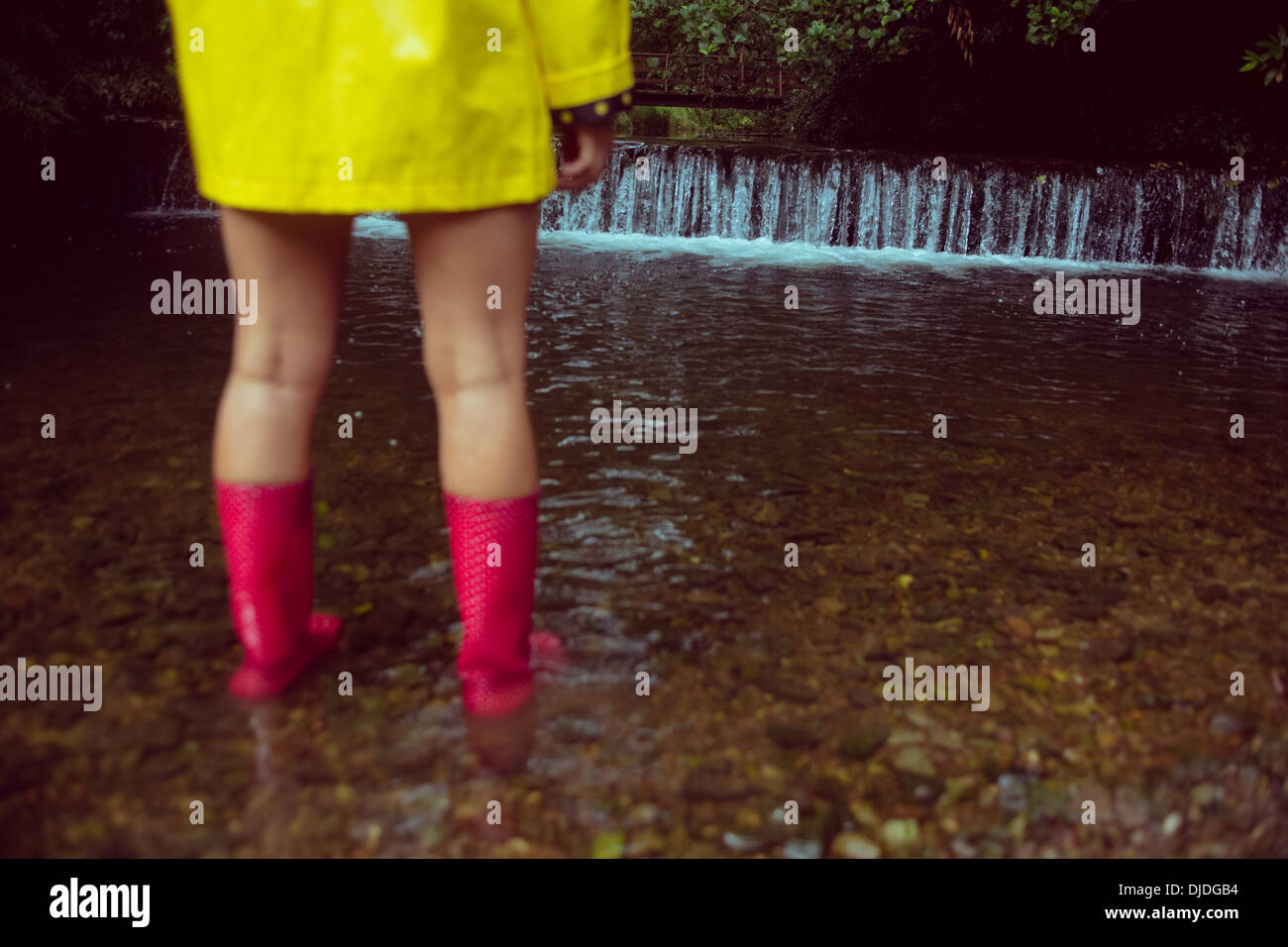 Woman in yellow raincoat and red gumboots in water Stock Photo
