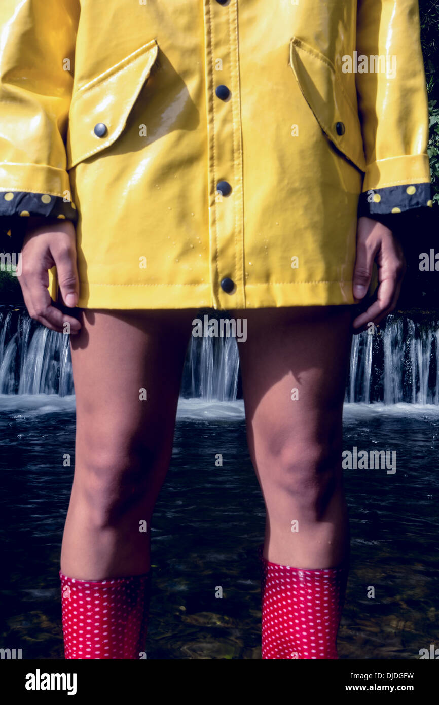 Woman in yellow raincoat and red gumboots against waterfall Stock Photo