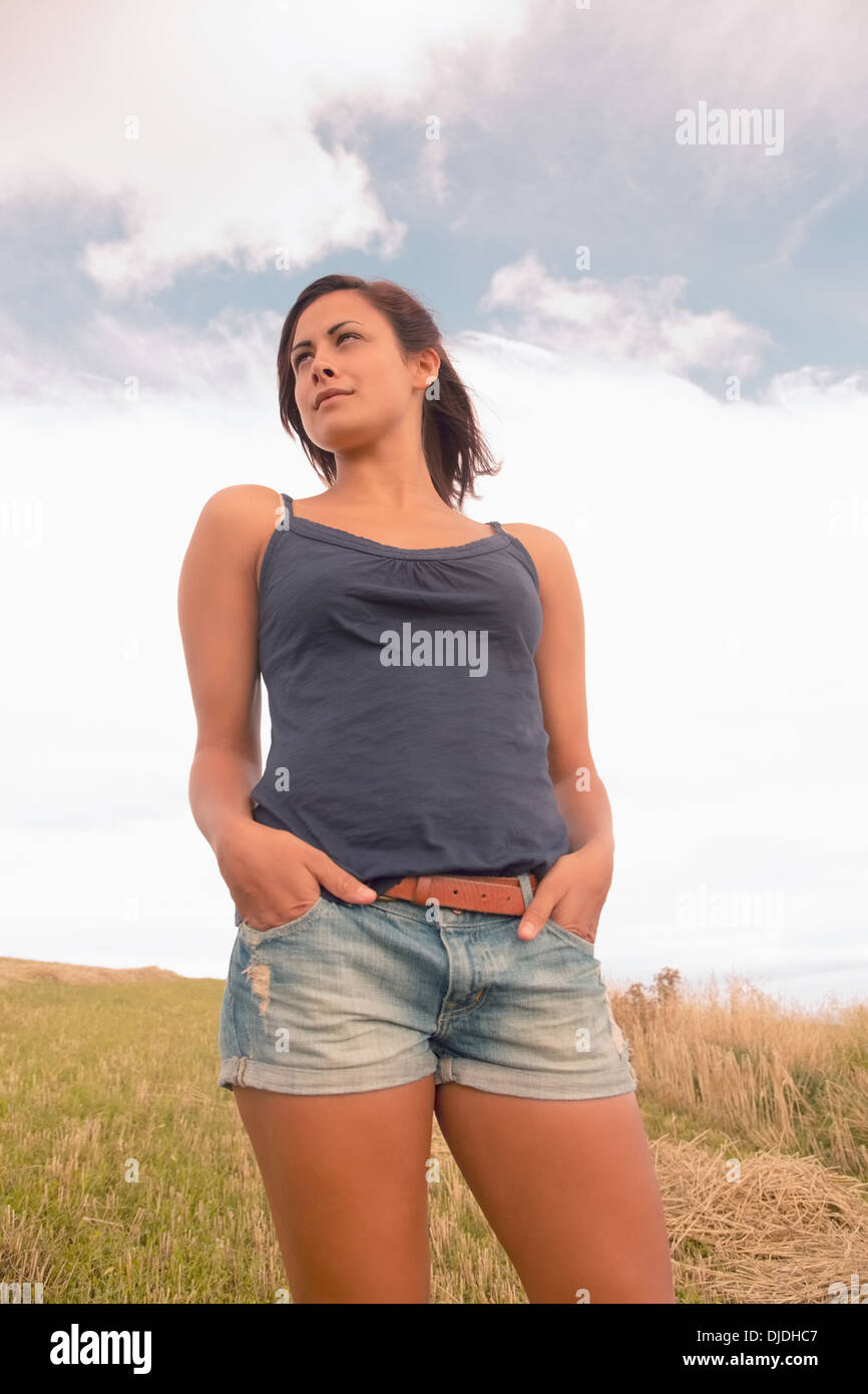 Woman in tank top and denim shorts on field against the sky Stock Photo