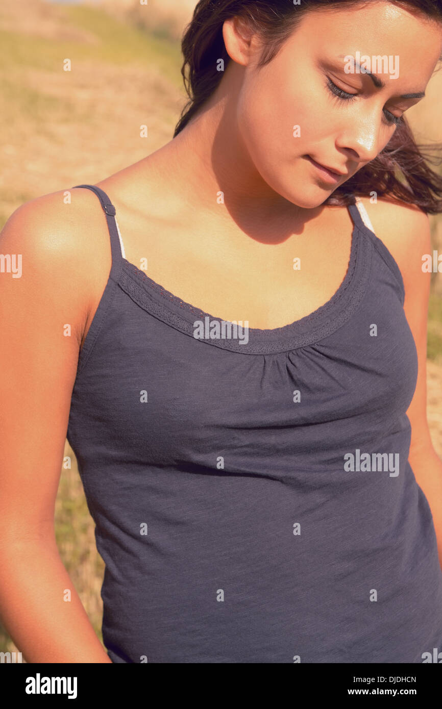 Thoughtful woman in tank top looking down at field Stock Photo