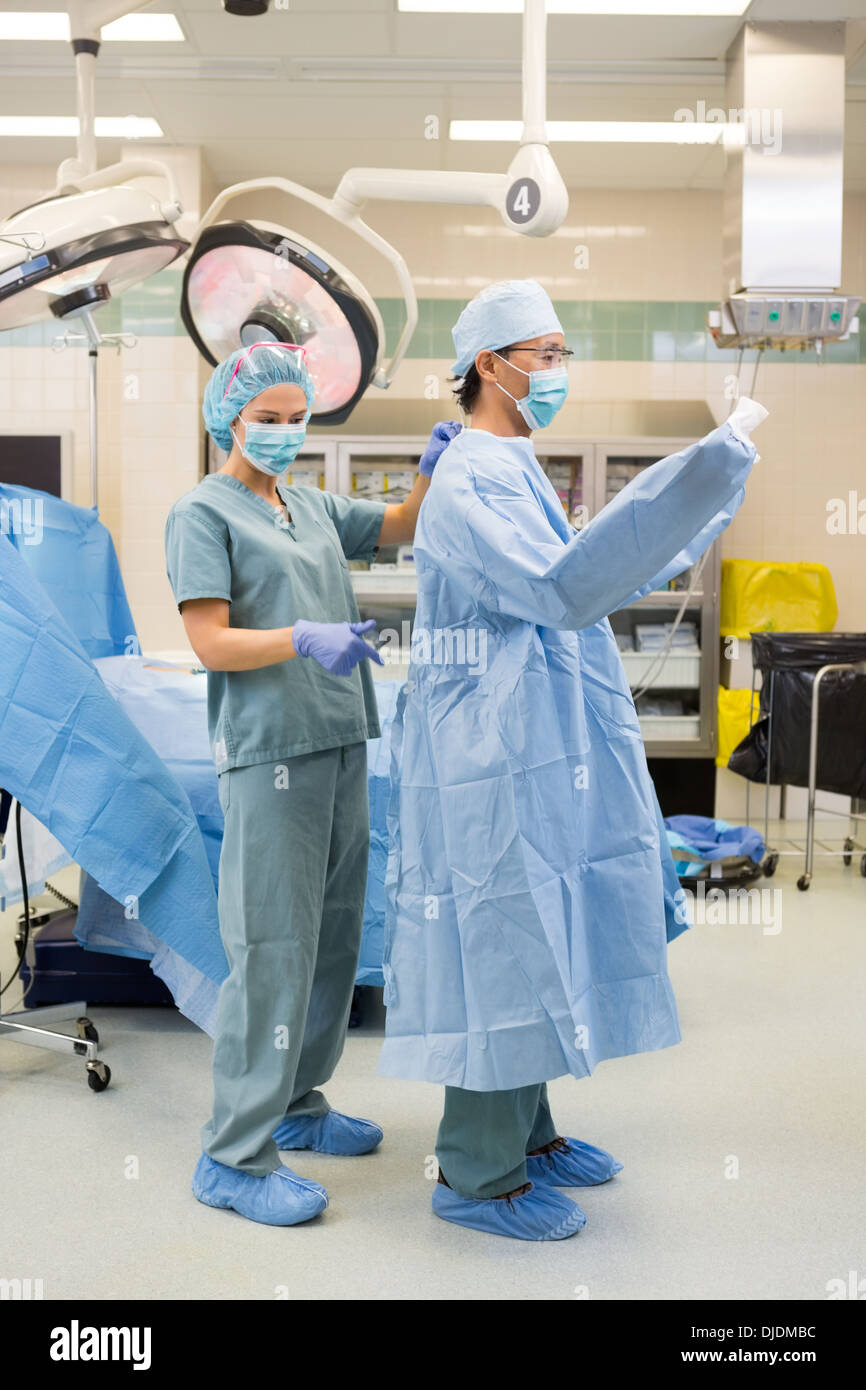Nurse Assisting Doctor In Wearing Operation Gown Stock Photo