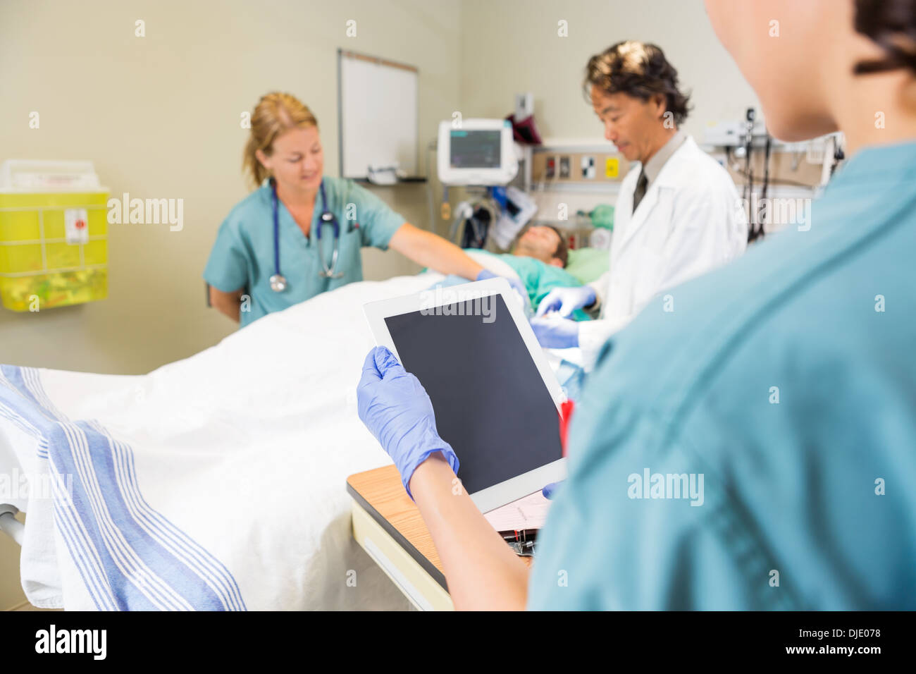 Nurse Holding Digital Tablet While Doctor And Colleague Treating Stock Photo