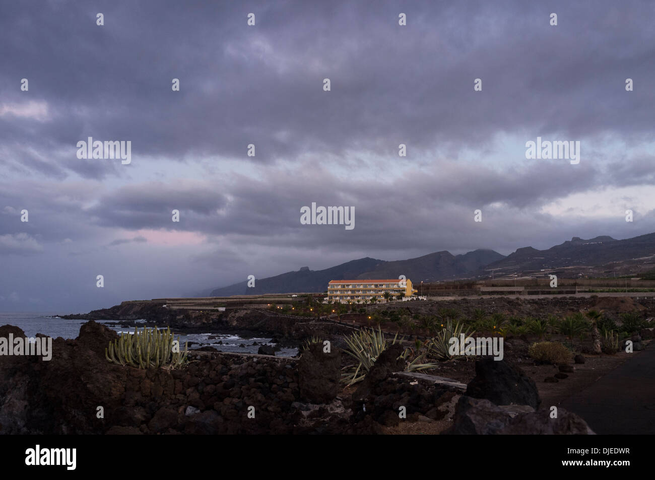 Apartment block on the coast at Las Salinas, Playa San Juan, Tenerife, at dawn with dramatic sky and Los Gigantes cliffs, Canary Stock Photo