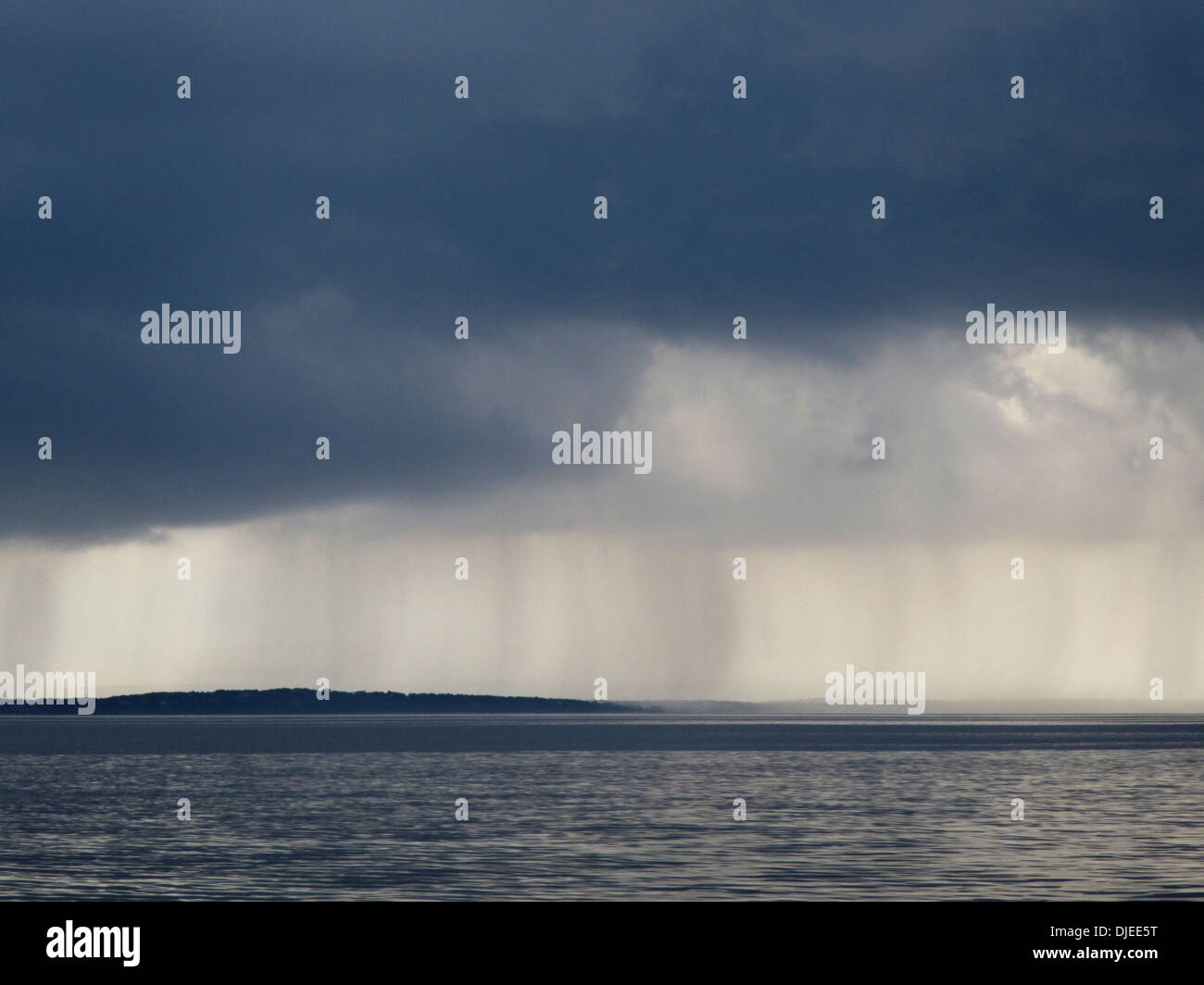 Visible rain falling from dark clouds over the ocean. Stock Photo