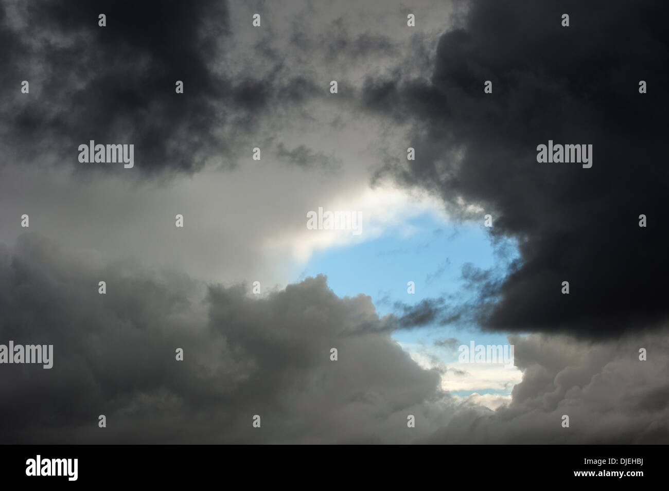 A break in thick layer of clouds of rain cloud showing patch of blue sky after thunderstorm Stock Photo