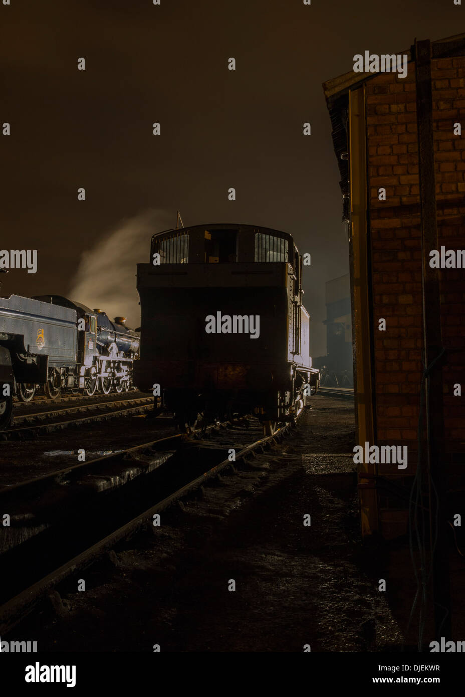 A GWR tank locomotive and 4-6-0 No.6023 King Edward II in steam and lit in silhouette at the GWR Society at Didcot at night Stock Photo