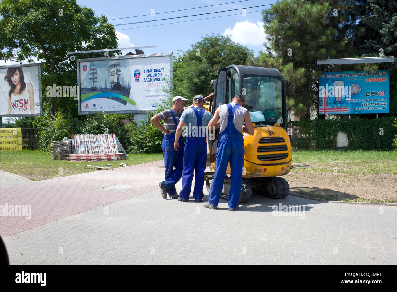 Men wearing blue suspender like trouser uniforms working with a tracked construction vehicle.  Warsaw Poland Stock Photo