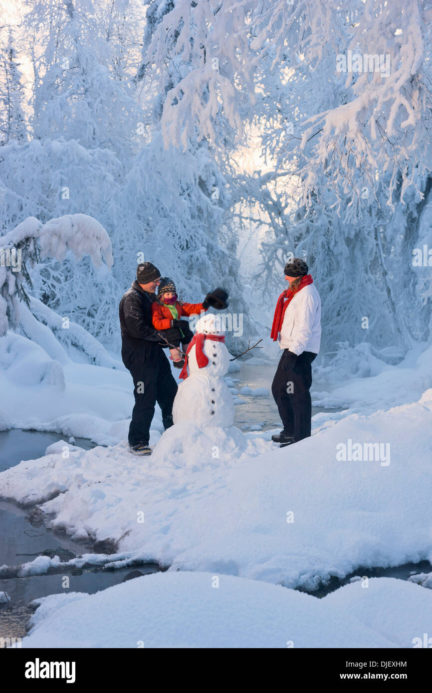 Family Putting A Top Hat On A Snowman Next To A Small Stream In A Hoarfrost Covered Forest Russian Jack Springs Park Anchorage Stock Photo