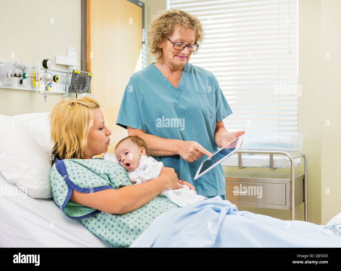 Nurse Explaining Reports On Digital Tablet To Woman With Babygir Stock