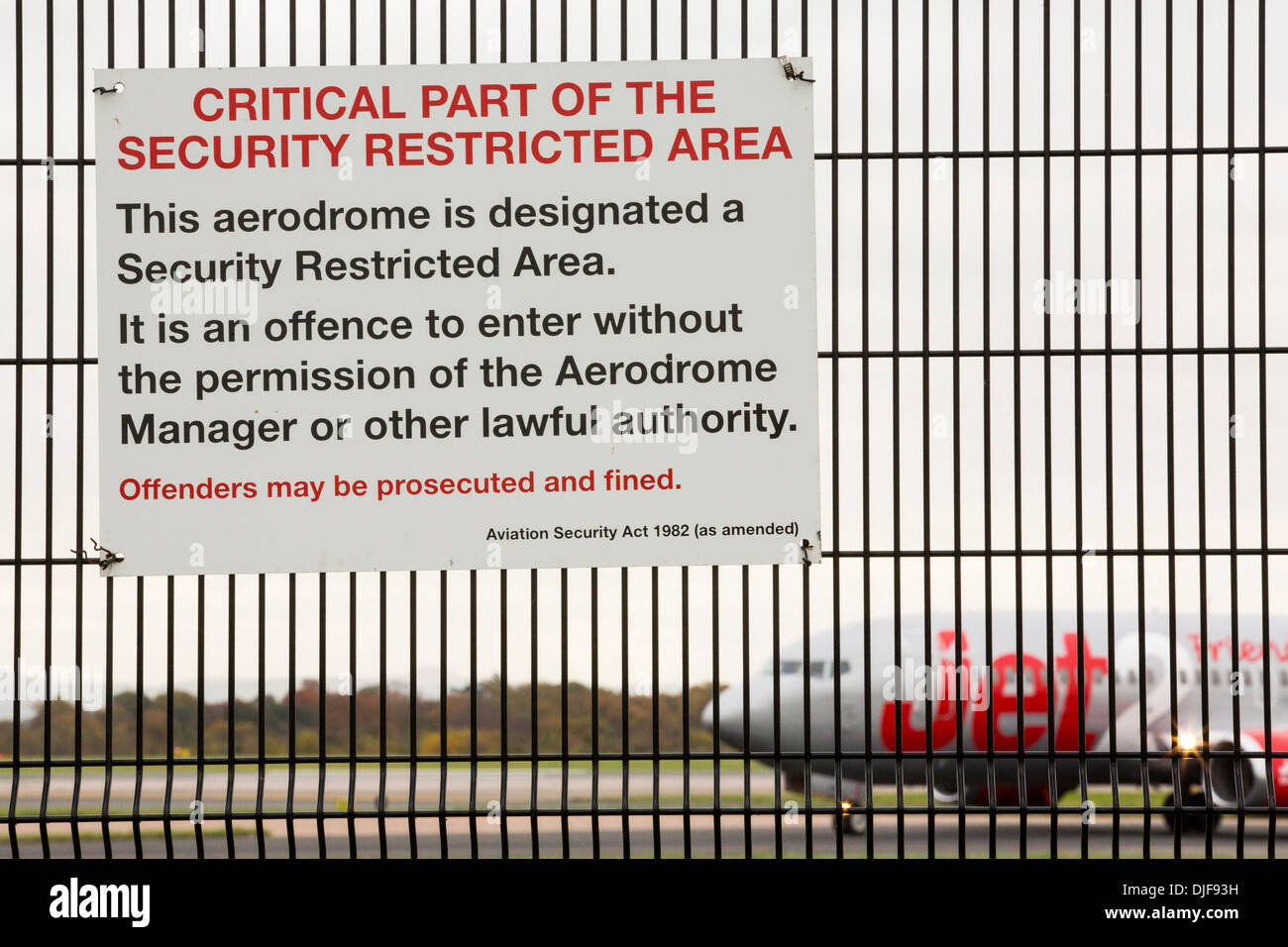 Signs on security fencing at Manchester Airport, UK with a plane behind