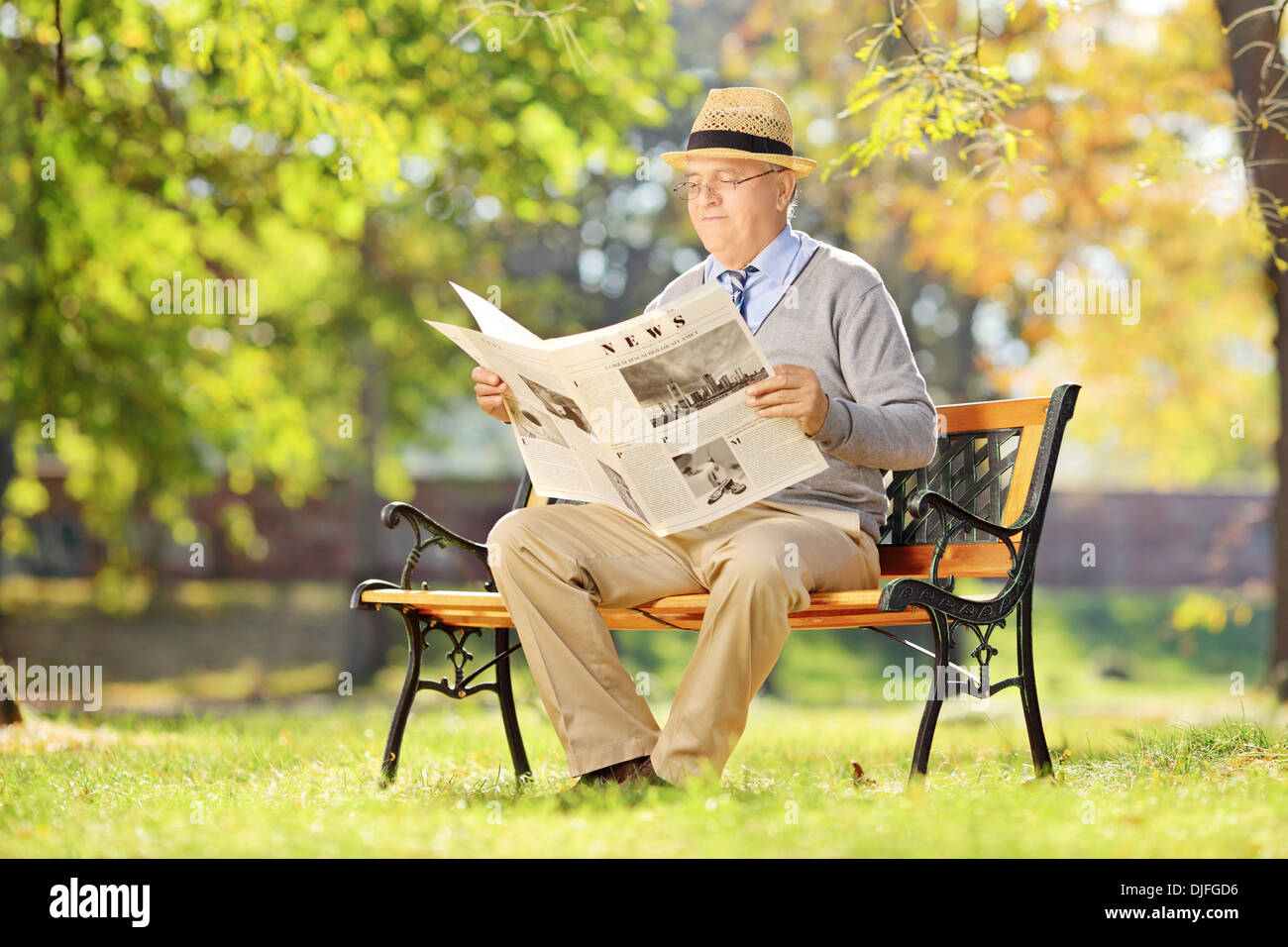 Senior man sitting on a bench and reading a newspaper in autumn Stock ...