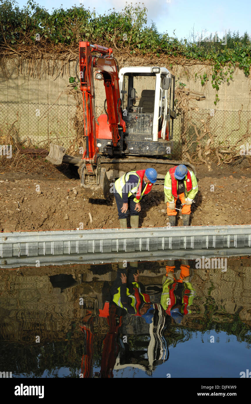 construction  workers examining canal bank repair with digging machine behind them Stock Photo