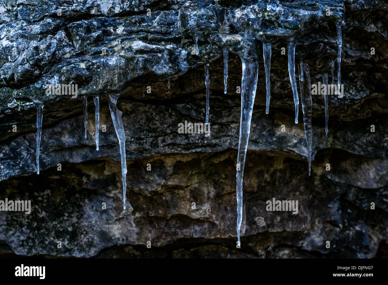 Photograph of an icicle formation hanging from the edge of a dark granite rock. Stock Photo