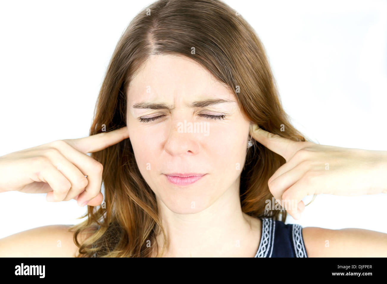 A young woman holds her hands over her ears to block out irritating sounds. Stock Photo