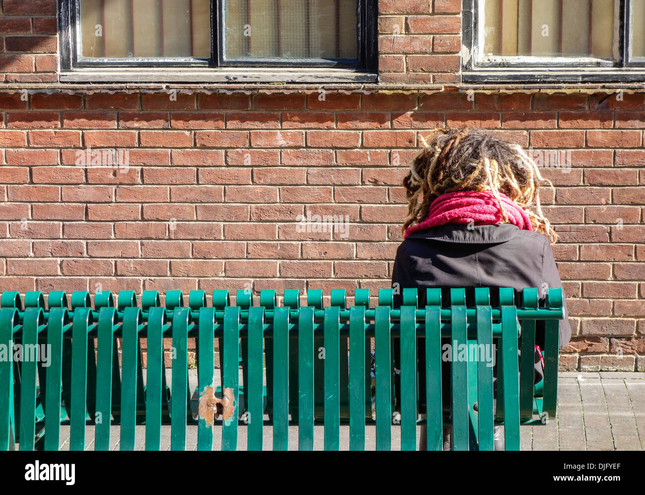 Young person with Dreadlocks sitting on bench Stock Photo