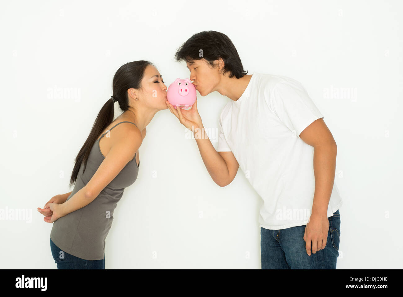 A young Asian couple holding a piggy bank and kissing it, a financial saving plan concept. Stock Photo