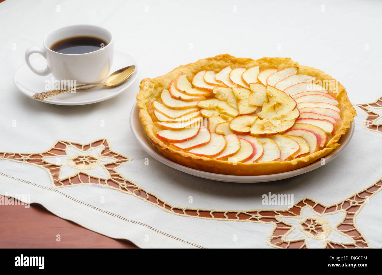 A tasty golden homemade apple tart and a cup of black coffee on an embroidered tablecloth Stock Photo