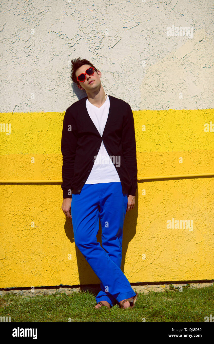A young man wearing a black sweater, white shirt, and blue pants, standing against a bright neon yellow wall, a fashion concept Stock Photo