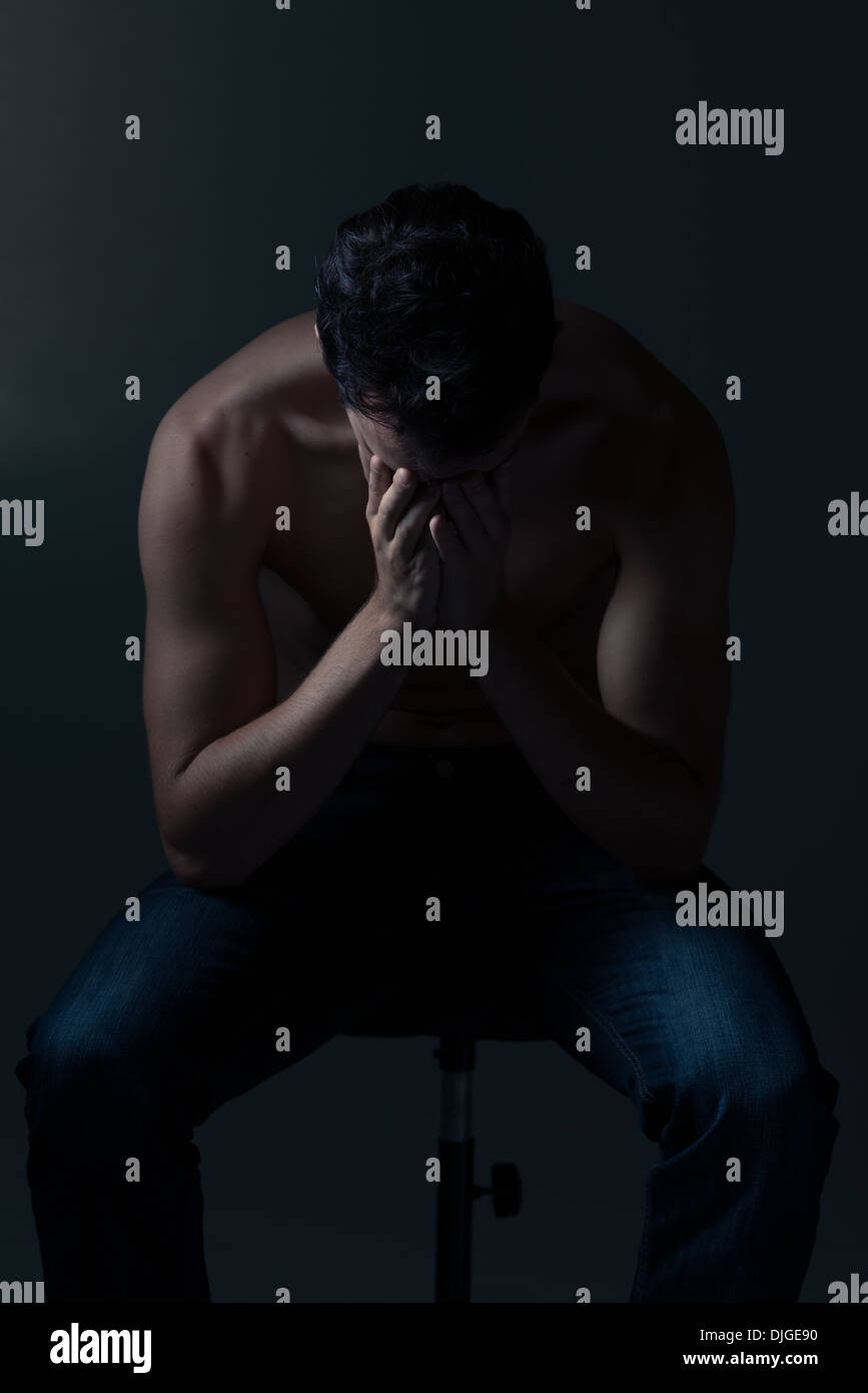 Young white Caucasian man bare chested sitting on a tool hunch over covering face with hands depressed, frustrated Stock Photo