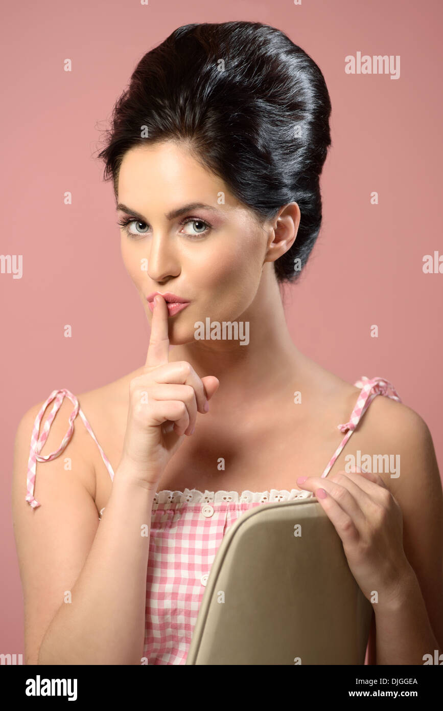 Beautiful woman holding a finger to her lips ,keeping a secret. A vintage style portrait with pink background, creative concept. Stock Photo
