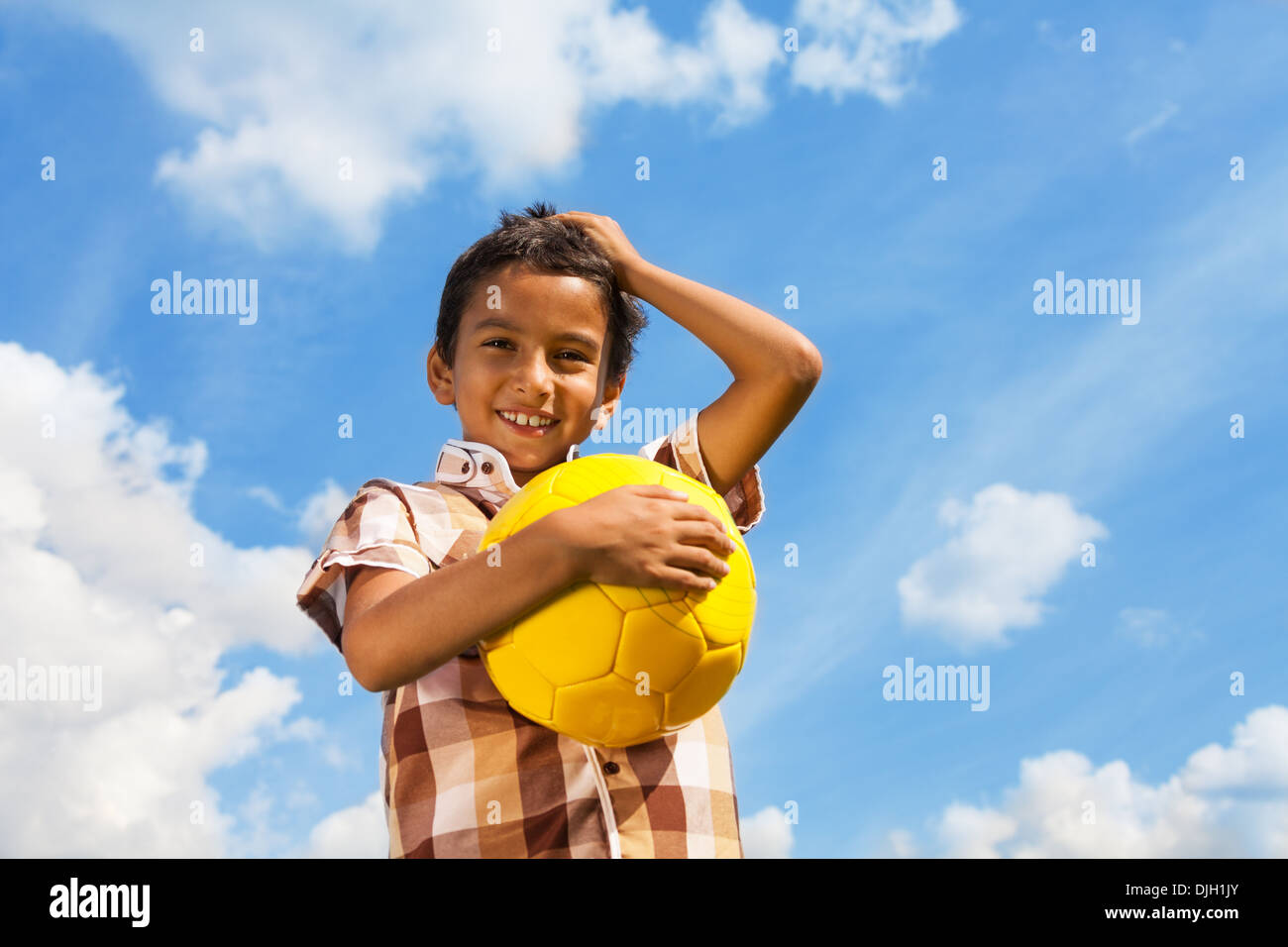 Happy smiling boy with soccer ball holding head with hand on sky background Stock Photo