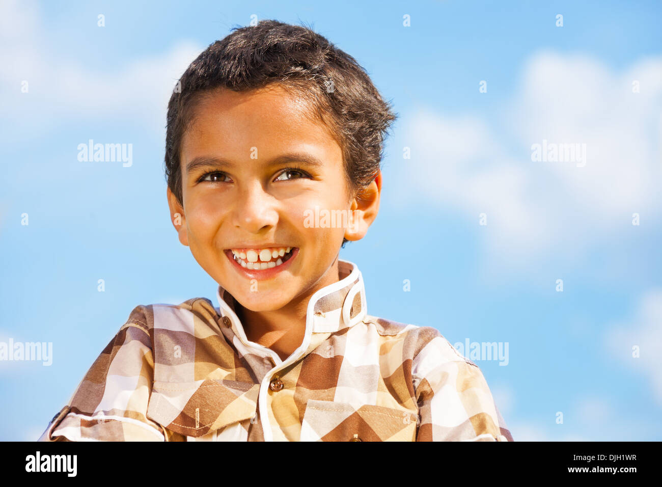 Laughing dark little 6 years old boy with short hair over blue sky Stock Photo