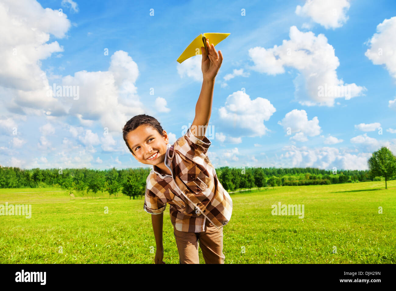 Happy boy leaning and throwing yellow paper airplane on bright sunny day in the field Stock Photo