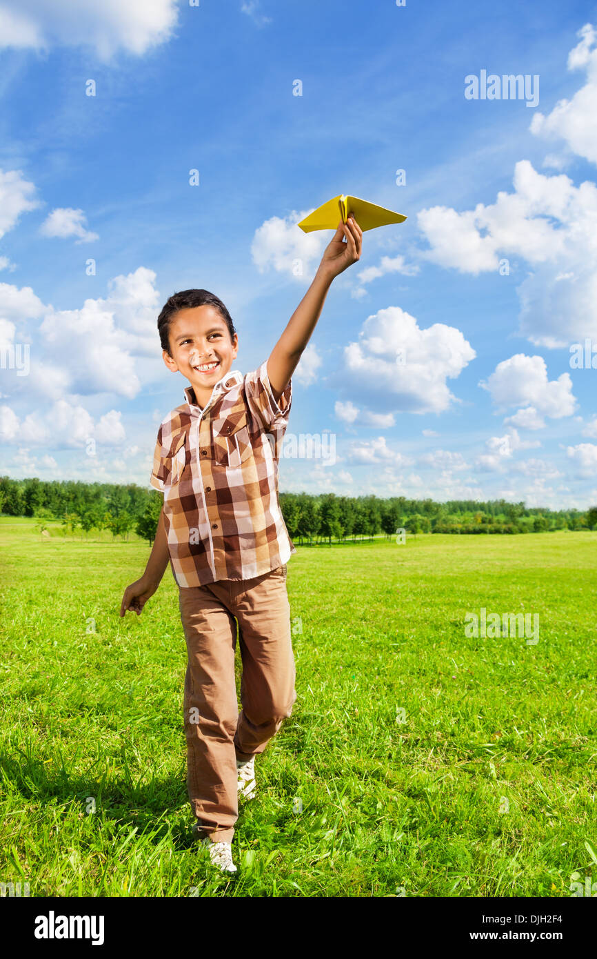 Happy boy throwing paper plane running in the park on sunny day Stock Photo