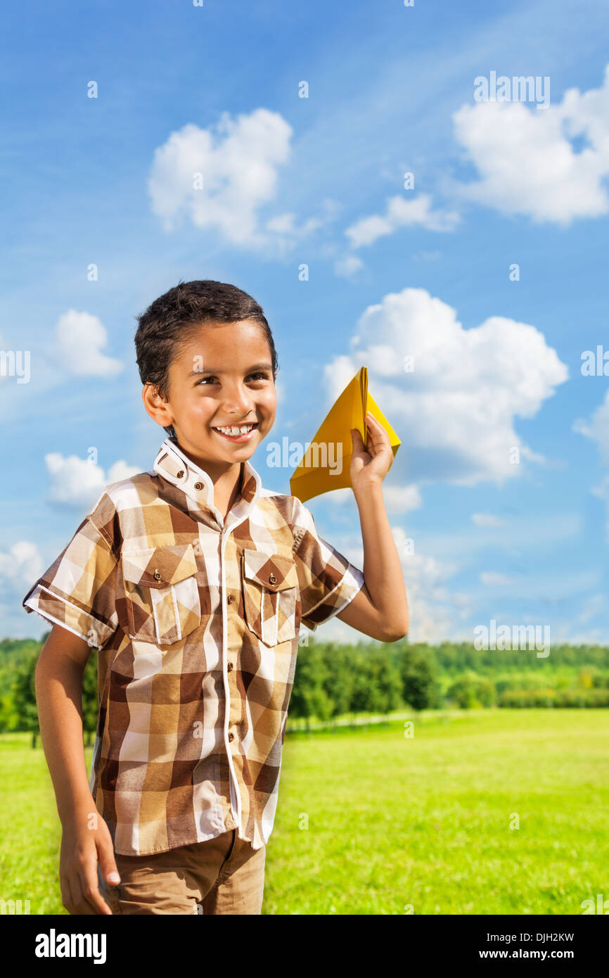 Cute little 6 years old boy holding blue paper airplane on bright sunny day Stock Photo